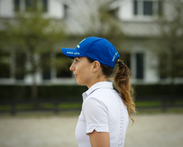 girl wearing white polo shirt and blue hat in front of white barn