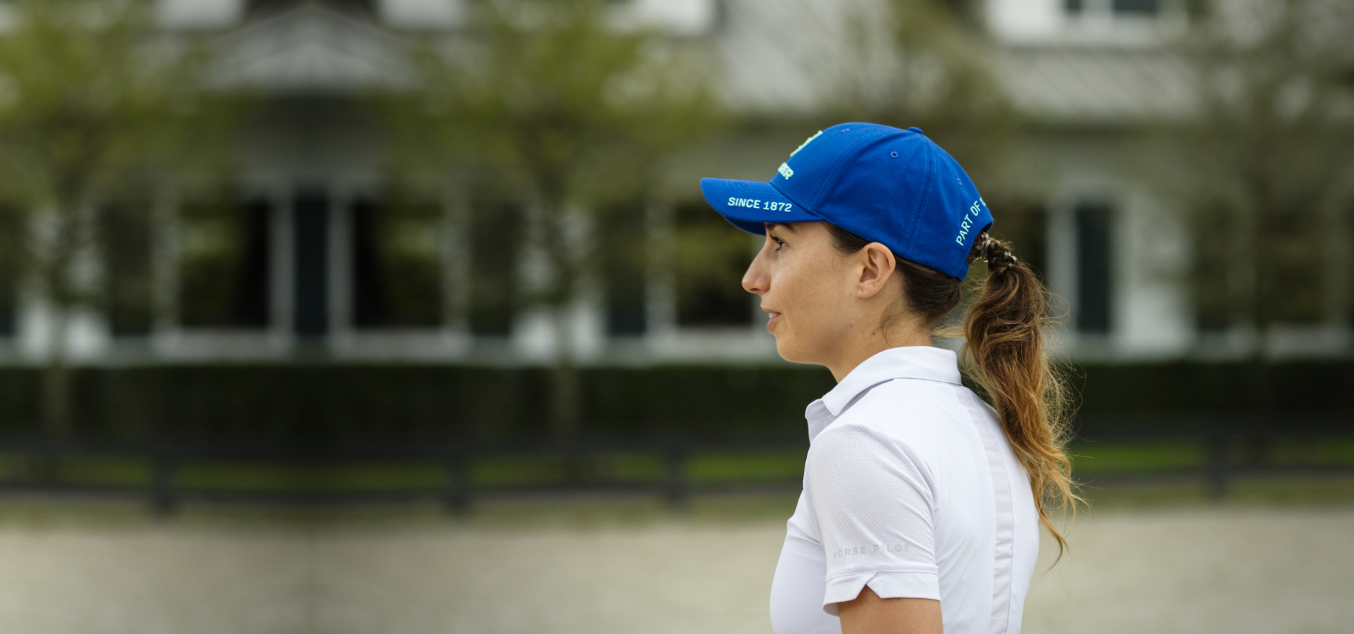 girl wearing white polo shirt and blue hat in front of white barn